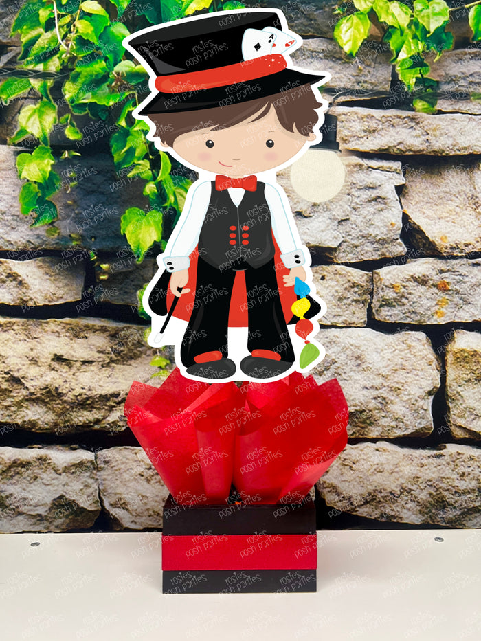 Kids birthday party magician themed centerpieces. The centerpieces feature illustrated cutouts including playing cards, a white rabbit in a tuxedo, a girl magician, a boy magician, a rabbit popping out of a top hat, and a magician's hat with a wand. Each cutout is set in a red, white, or black base filled with matching tissue paper. Receive fully assembled like pictured.