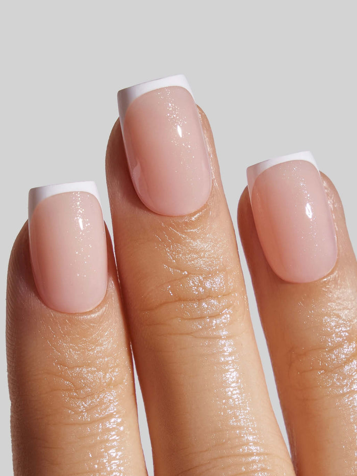 Close-up of a hand with nude color and white tip press-on nails on a neutral background