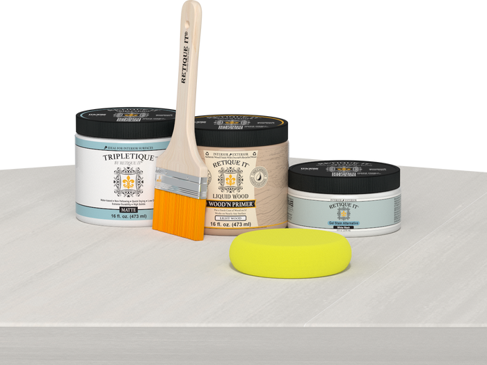 Retique It® White Wash Multipurpose Kit contents with Liquid Wood primer, White Wash gel stain alternative, Tripletique matte interior top coat, paintbrush, and yellow sponge displayed on a white wood surface.