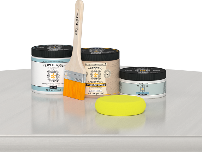 Retique It® White Wash Multipurpose Kit contents with Liquid Wood primer, White Wash gel stain alternative, Tripletique gloss interior top coat, paintbrush, and yellow sponge displayed on a white wood surface.