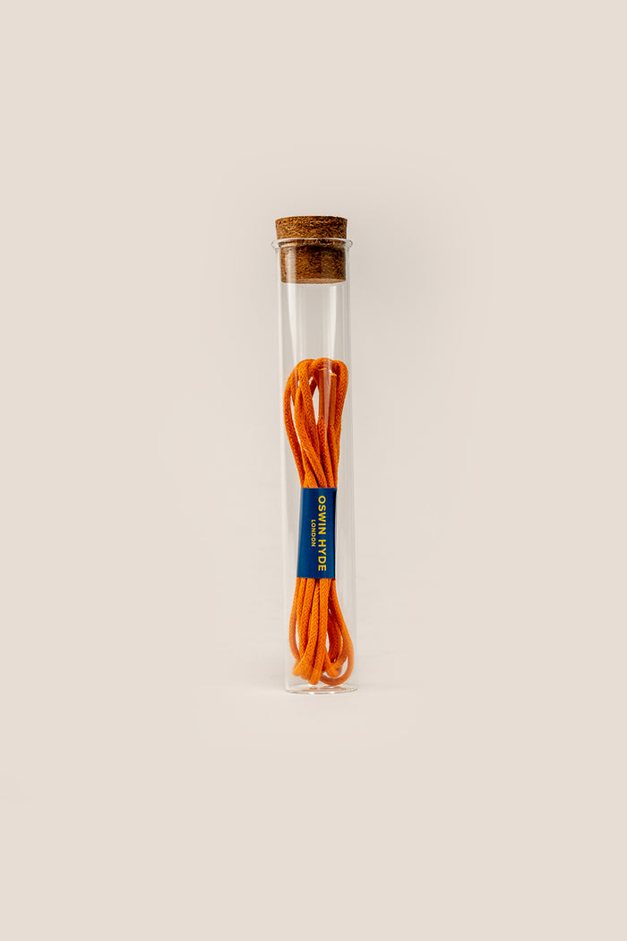Bright orange waxed cotton shoe laces polished with beeswax, neatly coiled and displayed in an Oswin Hyde glass tube.