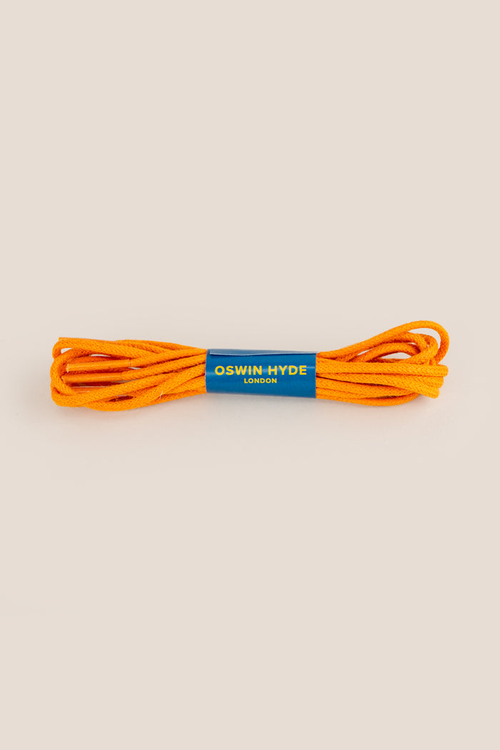 Bright orange waxed cotton shoe laces polished with beeswax, neatly coiled and displayed in an Oswin Hyde glass tube.