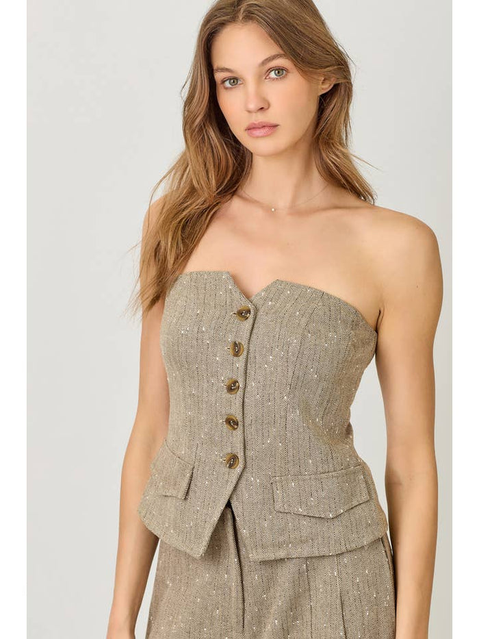 Woman wearing a beige strapless outfit with button details on a plain background